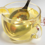 A glass of saffron detox water with vibrant golden color, garnished with lemon slices and mint leaves.