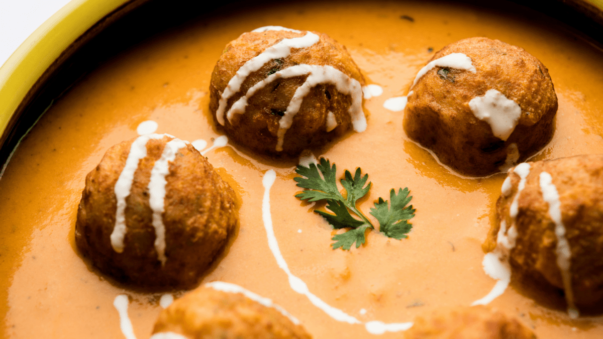 Zafrani Kofta Curry garnished with saffron and nuts in a creamy sauce.