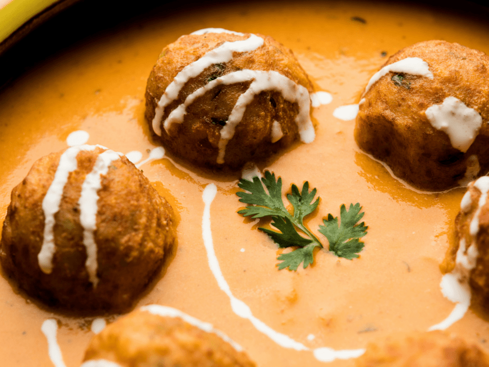 Zafrani Kofta Curry garnished with saffron and nuts in a creamy sauce.
